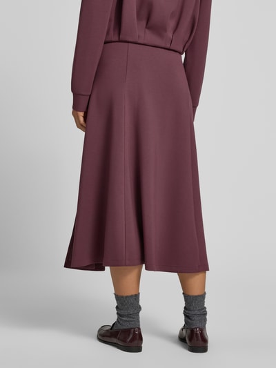 Frauenmodel trägt Midirock mit elastischem Bund von Christian Berg Woman in Bordeaux, lockere Passform, glatte Textur, Ganzkörperansicht Rückansicht. Midirock mit Modal-Anteil, Midilänge, Bundweite bei Größe S 80 cm.