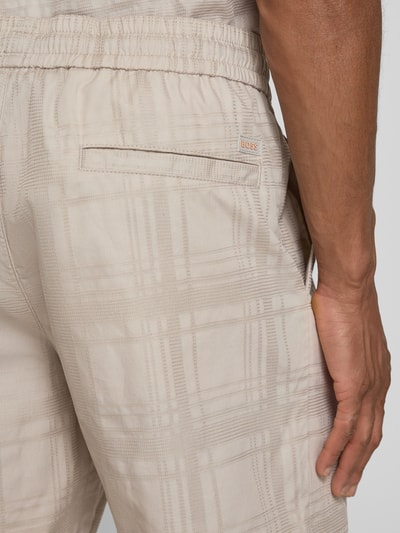 Männermodel trägt Tapered Chinoshorts aus reiner Baumwolle Modell 'SANDREW_6_SHORTS' von BOSS Orange in Beige mit Strukturmuster, Nahaufnahme Rückansicht.