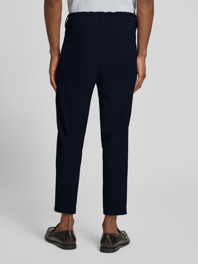 Męski model nosi Hose mit Eingrifftaschen Modell 'CHASY' od Drykorn, czarny, materiał z domieszką wiskozy, krój tapered fit, gładka tekstura, elastyczny pas, widoczne kieszenie, szerokość w rozmiarze 32/32: 42 cm, długość wewnętrzna nogawki: 66 cm, widok całej sylwetki z tyłu.