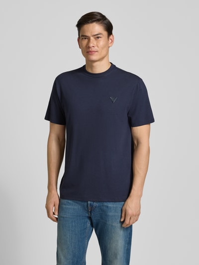 Männermodel trägt T-Shirt mit Logo und Rundhalsausschnitt von Guess in Dunkelblau aus Baumwoll-Mix, Relaxed Fit, Ganzkörperansicht von vorne.