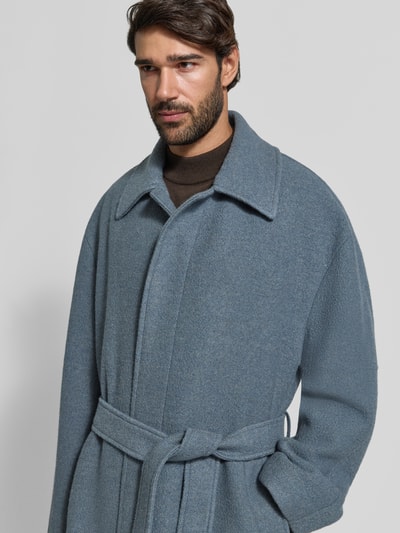 Männermodel trägt Wollmantel mit Bindegürtel von BOSS in Uni-Optik, Umlegekragen, verdeckte Knopfleiste, Nahaufnahme Oberkörper.