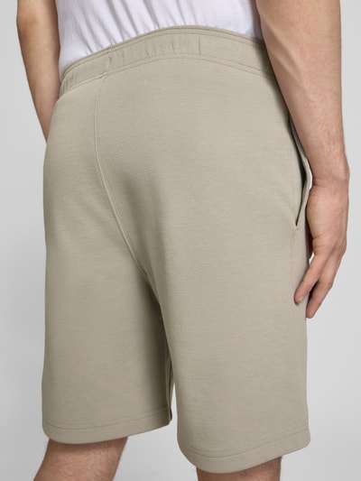 Męski model nosi Shorts mit Label-Stitching mit elastischem Bund od CHAMPION, bawełniany miks, krój regular fit, szerokość w rozmiarze M 37 cm, długość wewnętrzna nogawki 42 cm, ujęcie całej sylwetki z tyłu.