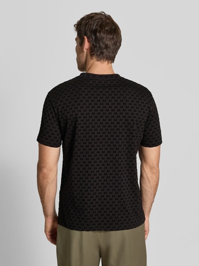 Męski model nosi Regular Fit T-Shirt mit Allover-Print von Armani Exchange, czarny z nadrukiem na całej powierzchni, krój regular fit, okrągły dekolt, z krótkim rękawem, długość tyłu w rozmiarze M: 63 cm, Ganzkörperansicht Rückansicht.