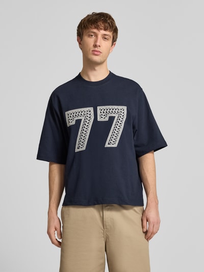 Männermodel trägt T-Shirt mit Ketten-Stickerei und Rundhalsausschnitt von REVIEW, Relaxed-Fit, Reine Baumwolle, Ganzkörperansicht von vorne.