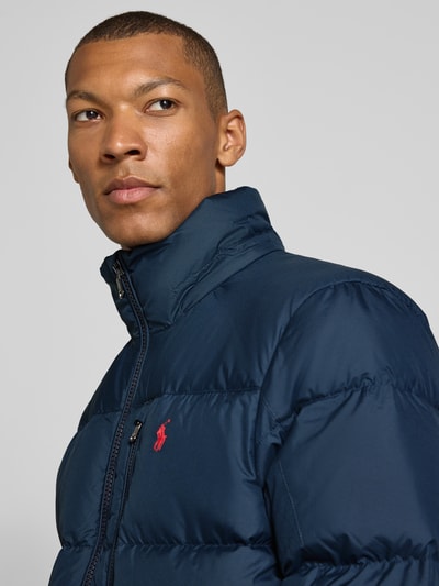 Männermodel trägt dunkelblaue Regular Fit Daunenjacke mit Logo-Stitching von Polo Ralph Lauren, glatte Struktur, Nahaufnahme Oberkörper. Herren Daunenjacke von Polo Ralph Lauren.