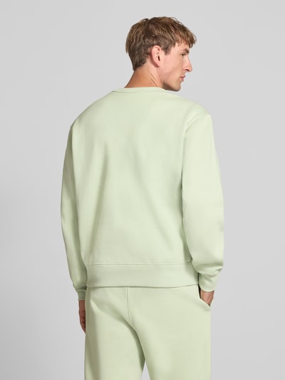 Männermodel trägt Sweatshirt mit Label-Details von Champion in Pastellgrün, lockere Passform, Baumwoll-Mix, Rückenansicht, ganzkörperansicht.
