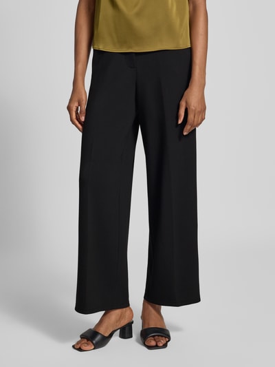 Kobiece model prezentuje czarne spodnie szerokie krój regular fit z mieszanki modalu model 'BELLIS' od VERO MODA, zbliżenie na dolną część ciała.