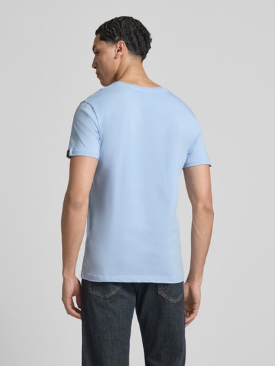 Mężczyzna model nosi jasnoniebieski męski t-shirt z detalem z logo, prosty krój, bawełna, Alpha Industries, model 'BASIC', okrągły dekolt, długość tyłu w rozmiarze M: 69 cm, całkowite ujęcie z tyłu.