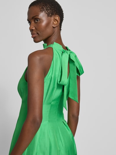Frauenmodel trägt Cocktailkleid mit Drapierungen Modell 'Miller' von Forever New aus Viskose-Leinen-Mix in A-Linie, Midikleid, kräftiges Grün, mit Neckholder und rückseitiger Schnürung, Glanzoptik, Detailaufnahme Rückansicht.