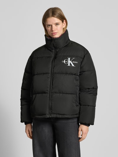 Modelka nosi Jacke mit Logo-Print od Calvin Klein Jeans, czarny kolor, prosty krój, stójka, nadruk logo, elastyczne mankiety, widok całej sylwetki z przodu, długość pleców w rozmiarze M: 66 cm, szerokość ramion w rozmiarze M: 63 cm, szerokość klatki piersiowej w rozmiarze M: 60 cm, długość rękawa w rozmiarze M: 63 cm