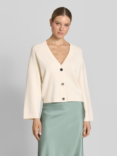 Frauenmodel trägt Strickjacke aus Viskose-Mix mit V-Ausschnitt von comma, cremefarben, Relaxed Fit, Knopfleiste, Ganzkörperansicht von vorne.