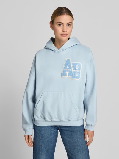 Frauenmodel trägt Relaxed Fit Hoodie mit Logo-Detail von Anine Bing aus reiner Baumwolle in Hellblau, Känguru-Tasche, elastische Abschlüsse, Rückenlänge bei Größe S 85 cm, Ganzkörperansicht von vorne.