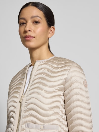 Frauenmodel trägt Slim Fit Steppjacke mit aufgesetzten Taschen Modell 'Tamina' von SAVE THE DUCK in Beige, Nahaufnahme Oberkörper, Stepp-Optik, Reißverschluss, Rundhalsausschnitt