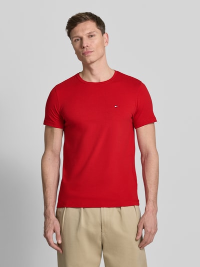 Männermodel trägt Slim Fit T-Shirt aus Baumwoll-Mix von Tommy Hilfiger in Rot, unifarben, kurzarm, Logo-Detail, Ganzkörperansicht von vorne.