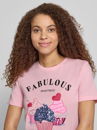 Frauenmodel trägt Damen T-Shirt von Only, Modell 'Shaped Fit T-Shirt aus reiner Baumwolle Modell 'KITA'' in Optik: Unifarben mit Motiv-Print, Pailletten, Strasssteine, Rundhals, Kurzarm aus Jersey, Material: reine Baumwolle, zarte Rosa- und Pastellfarben, Nahaufnahme Oberkörper.