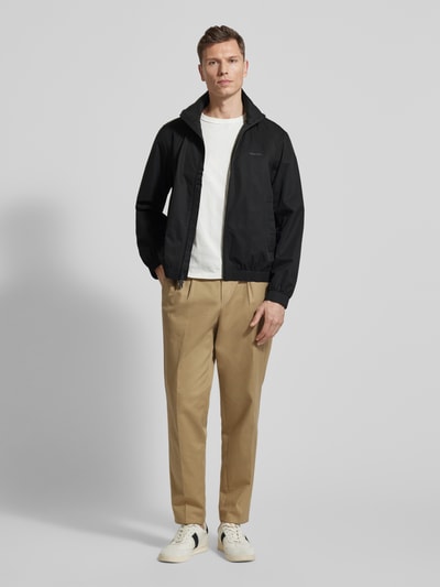 Männermodel trägt Jacke mit Stehkragen und Reißverschluss von CK Calvin Klein in Schwarz, kombiniert mit heller Hose, Ganzkörperansicht von vorne. Regular Fit, Reißverschluss, Eingrifftaschen, Rückenlänge 65 cm, Schulterbreite 46 cm, Brustweite 57 cm, Ärmellänge 67 cm.