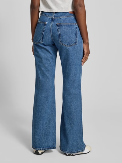 Frauenmodel trägt Flared Fit Jeans im 5-Pocket-Design von Anine Bing aus reiner Baumwolle mit Logo-Detail, Knopf-Reißverschluss, mittleres Jeansblau, strukturierte Oberfläche, Ganzkörperansicht Rückansicht.