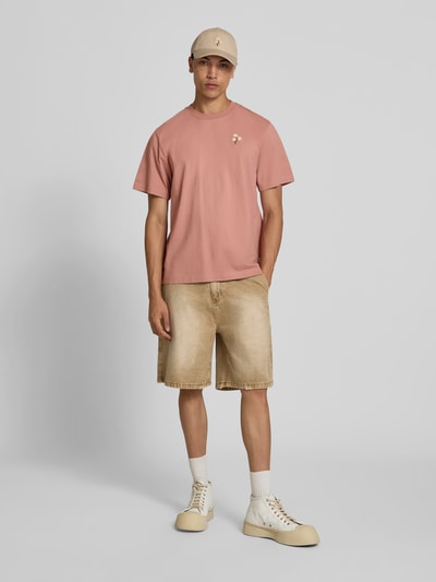 Männermodel trägt T-Shirt mit Rundhalsausschnitt von Forét, Reine Baumwolle, Regular-Fit, florales Stitching, Kurzärmelig, Beige- und Rosatöne, Rückenlänge bei Größe M: 67 cm, Ganzkörperansicht von vorne.