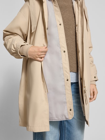 Vrouwenmodel draagt Regular fit lange jas met tweewegritssluiting model 'Joy' van g-lab in beige, elastische mouwboord, capuchon met tunnelkoord, ruglengte maat S 94 cm, schouderbreedte 57 cm, borstwijdte 64 cm, mouwlengte 57 cm, detailopname bovenlichaam.
