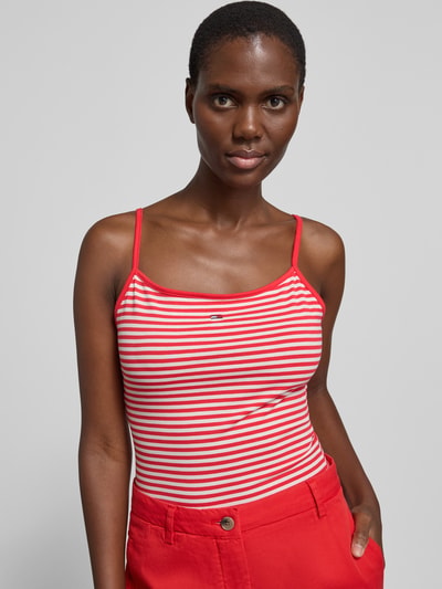 Frauenmodel trägt Slim Fit Trägertop aus Baumwoll-Mix von Tommy Jeans mit Optik:Allover-Muster Gestreift, Logo-Stitching, Karree-Ausschnitt, Trägerform: Spaghettiträger, Materialverarbeitung: Jersey, Material: Baumwoll-Mix, Farben: Rot und Weiß, Nahaufnahme Oberkörper.