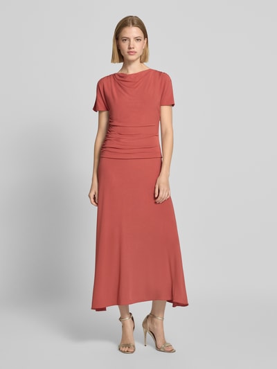 Frauenmodel trägt Cocktailkleid mit Wasserfall-Ausschnitt und Drapierungen von Christian Berg Cocktail in A-Linie, Midikleid, Ganzkörperansicht von vorne. Viskose-Elasthan-Mix, seitlicher Reißverschluss, sanfte Drapierungen, matter Rostton.
