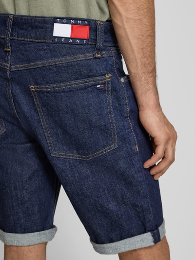 Männermodel trägt Regular Fit Jeansshorts aus Baumwoll-Mix von Tommy Jeans in dunkler Denim-Optik mit Label-Patch und Logo-Stitching, Detailaufnahme Rückenansicht.