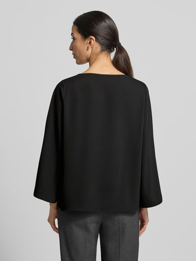 Modelka nosi Blusenshirt mit Rundhalsausschnitt von comma, czarny materiał z domieszką stretchu, luźny krój, długość tyłu 59 cm, długość rękawa 52 cm, widok całej sylwetki od tyłu.