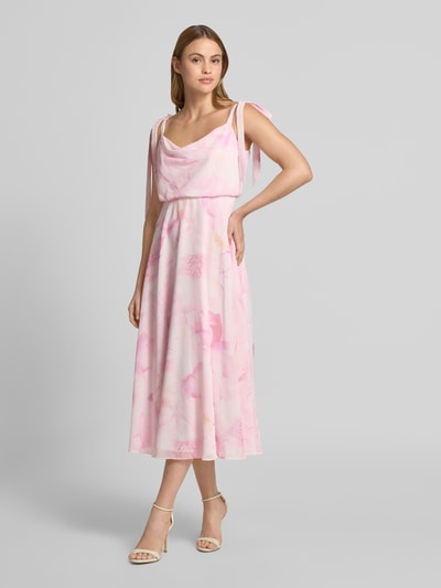 Frauenmodel trägt Knielanges Cocktailkleid mit floralem Allover-Print von Jake*s Cocktail in zarten Rosa- und Cremetönen, blickdichter Unterrock, taillierte Passform, Zierschleifen, ärmelloses Design, Ganzkörperansicht von vorne.