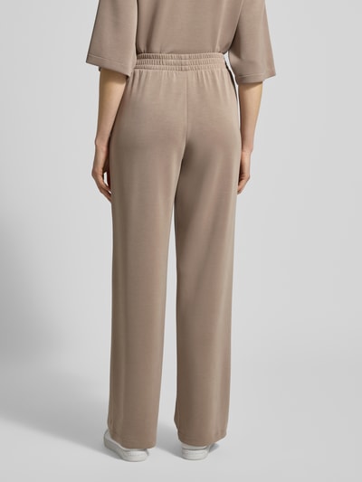 Kobiece modelka nosi Spodnie z mieszanki modalu z elastycznym pasem od Jake*s Casual, krój relaxed fit, wpuszczane kieszenie, szerokość w rozmiarze S 35 cm, długość wewnętrzna nogawki 79 cm, kolor beżowy, gładka tekstura, widok całej sylwetki z tyłu.