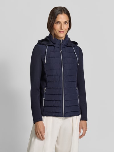 Vrouwenmodel draagt Steppjacke mit Kapuze und Reißverschlusstaschen van Christian Berg Woman Selection, donkerblauw, regular fit, gewatteerde structuur, witte broek, vooraanzicht van het hele lichaam. Ruglengte maat 36: 59 cm, schouderbreedte: 41 cm, borstwijdte: 50 cm, mouwlengte: 65 cm.