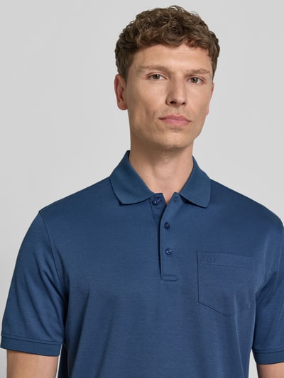 Männermodel trägt Regular Fit Poloshirt mit Brusttasche und Label-Stitching von bugatti in Blau, Knopfleiste, Polokragen, Nahaufnahme Oberkörper. Herren Poloshirt, Rückenlänge bei Größe M: 70 cm.
