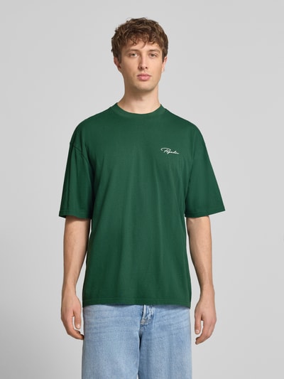 Męski model nosi Oversized T-Shirt aus reiner Baumwolle Modell 'Pike' od Pegador, zielony, wyhaftowane logo, okrągły dekolt, krój oversized, długość tyłu w rozmiarze M: 71 cm, widok całej sylwetki z przodu.