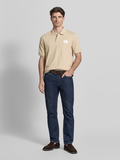 Männermodel trägt Regular Fit Poloshirt mit Knopfleiste von ARMANI EXCHANGE aus Baumwoll-Elasthan-Mix in Beige, Label-Print, elastische Ärmelbündchen, Rückenlänge 70 cm bei Größe M, Ganzkörperansicht von vorne.