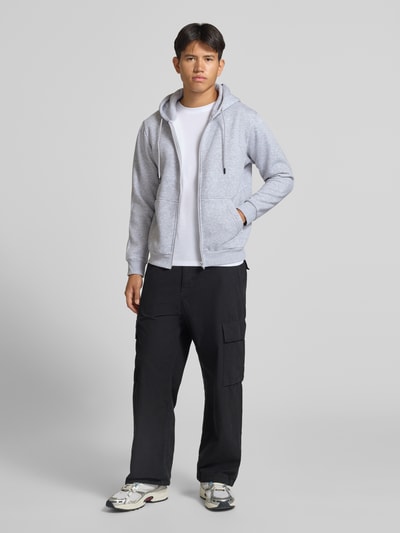 Männermodel trägt Regular Fit Sweatjacke aus Baumwoll-Mix Modell 'BRADLEY' von JACK & JONES in Hellgrau, Ganzkörperansicht von vorne. Baumwoll-Mix, Kapuze mit Tunnelzug, getrennte Känguru-Tasche, elastische Abschlüsse, Rückenlänge 67 cm, Ärmellänge 68 cm.