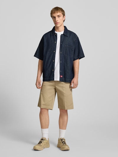 Männermodel trägt Relaxed Fit Jeanshemd mit Brusttasche von Dickies in donkerblauw, katoen, kentkraag, borstzak, label-patch, casual look, ganzkörperansicht von vorne