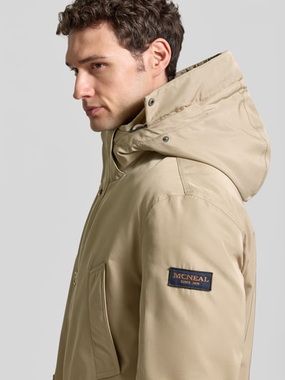Männermodel trägt Parka mit Kapuze und Pattentaschen von MCNEAL in Beige, sichtbares Markenlogo, glatte Textur, Nahaufnahme Oberkörper. Kontext: Regular Fit, verdeckter Reißverschluss, Knopfleiste, Eingrifftaschen, Rückenlänge 85 cm, Schulterbreite 49 cm, Brustweite 46 cm, Ärmellänge 67 cm.