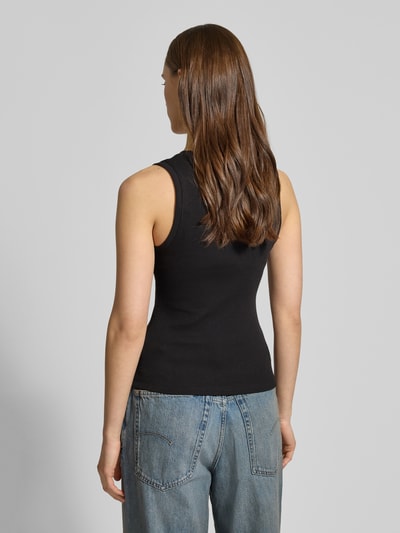Modelka nosi Slim Fit Tank Top aus Baumwoll-Mix od Tommy Jeans, czarna, jednokolorowa, krój slim fit, szerokie ramiączka, bawełniany miks, żebrowana faktura, logo, widok całej sylwetki z tyłu.