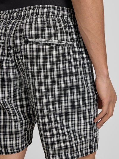 Männermodel trägt Shorts mit elastischem Bund Modell 'SLADE' von Redefined Rebel aus Reine Baumwolle mit Kordelzug, Detailaufnahme Rückansicht. Regular-Fit, Bundweite bei Größe M: 37 cm, Innenbeinlänge: 18 cm, schwarz-weiß kariertes Muster mit feiner Textur.