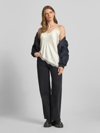 Vrouwenmodel draagt Shaped Fit Trägertop aus Satin Modell 'BELLA' van Only in effen crème met kant, V-hals, verstelbare spaghettibandjes, asymmetrische zoom, satijnstructuur, volledig lichaam van voren.