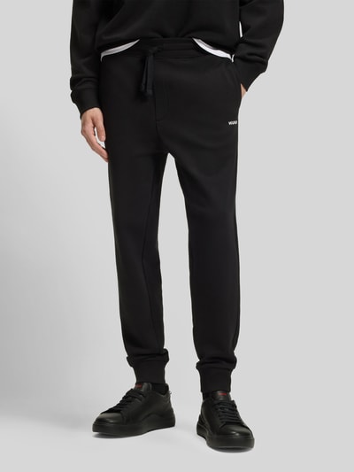 Männermodel trägt Regular Fit Jogginghose aus reiner Baumwolle Modell 'DAYOTE232' von HUGO in Schwarz mit Label Print, Nahaufnahme Unterkörper.