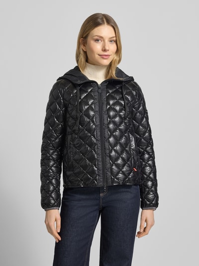 Frauenmodel trägt Regular Fit Jacke in Stepp-Optik Modell 'YOSIE' von Frieda & Freddies, schwarz, Kapuze mit Tunnelzug, Reißverschluss, Eingrifftaschen, Logo-Applikation, elastische Ärmelabschlüsse, Ganzkörperansicht von vorne. Rückenlänge 61 cm, Schulterbreite 46 cm, Brustweite 49 cm, Ärmellänge 60 cm.