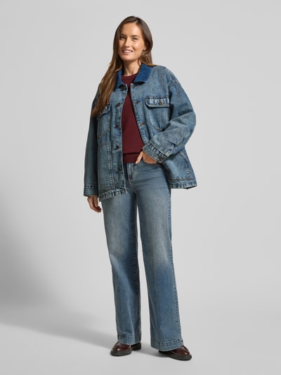 Frauenmodel trägt Kurtka jeansowa z bawełny, krój relaxed fit, wykładany kołnierz, listwa guzikowa, kieszenie na piersi, wpuszczane kieszenie, długość tyłu 61 cm, szerokość ramion 56 cm, szerokość klatki piersiowej 68 cm, długość rękawów 55 cm, model 'JOYBIRD' od American Vintage, niebieski denim, prosty fason, styl casual, całkowita sylwetka z przodu.