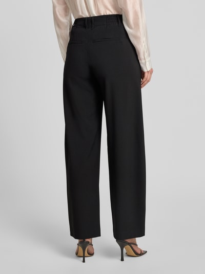 Frauenmodel trägt Wide-Fit Damen Stoffhose mit Viskose-Anteil Modell 'Dutiful' von Drykorn, Elastischer-Material-Mix, Gesäßtaschen, Haken-Reißverschluss, schwarze Farbe, glatte Textur, Ganzkörperansicht Rückansicht.