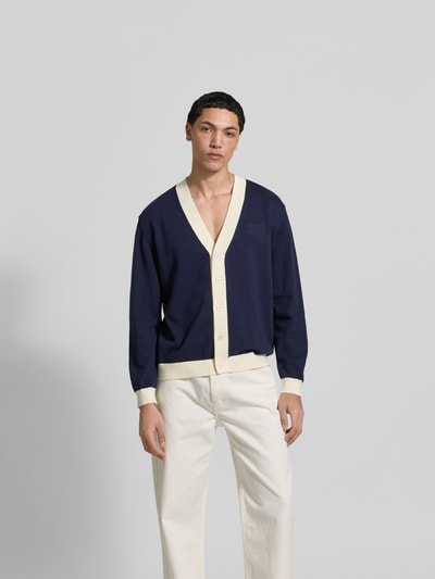 Männermodel trägt Cardigan aus reiner Baumwolle von MAISON KITSUNÉ in Dunkelblau mit cremefarbenen Details, lockere Passform, Ganzkörperansicht von vorne.