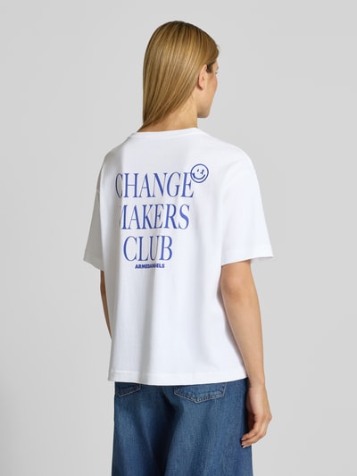 Frauenmodel trägt Oversized T-Shirt aus reiner Baumwolle Modell 'GIANNAA CHAANGE' von Armedangels, weiß, kurzarm, blauer Label Print, Rundhalsausschnitt, unifarbene Optik, Feinripp, Ganzkörperansicht Rückansicht.