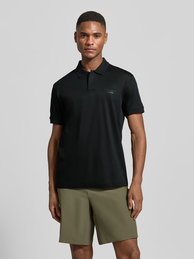 Männermodel trägt Regular Fit Poloshirt aus reiner Baumwolle Modell 'PS Spirit 70 Plk' von BOSS Green X PORSCHE, unifarben, Kurzarm, Ganzkörperansicht von vorne.