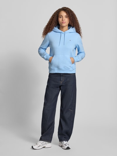Frauenmodel trägt Regular Fit Hoodie aus Baumwoll-Mix von Tommy Jeans in Optik: Unifarben mit Logo-Stitching, Ganzkörperansicht von vorne.
