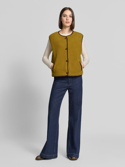 Vrouwenmodel draagt Relaxed Fit bodywarmer met doorlopende knoopsluiting van Christian Berg Woman, Teddybont, ronde hals, mouwloos, zijsteekzakken, mosterdgeel met bruine accenten, grovere textuur, Ganzkörperansicht von voren.