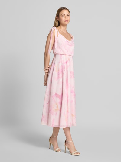 Frauenmodel trägt Knielanges Cocktailkleid mit floralem Allover-Print von Jake*s Cocktail in Rosa mit Zierschleifen, taillierter Passform und blickdichtem Unterrock, Ärmelloses-Design, fließende Textur, Ganzkörperansicht von vorne.