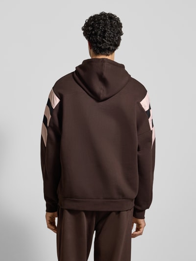 Männermodel trägt Hoodie mit Kapuze von adidas Originals in Braun mit rosa Details, Lockerer-Schnitt, Ganzkörperansicht Rückansicht. Rückenlänge bei Größe M: 71 cm, Ärmellänge bei Größe M: 66 cm, Label-Stitching, Känguru-Tasche, gerippte Abschlüsse.